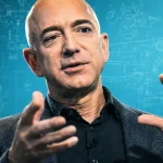 Jeff Bezos gestikuluje počas prezentácie na modrom technologickom pozadí s nákresmi a schémami, ktoré evokujú inovácie, umelú inteligenciu a veľké technologické vízie.