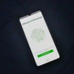 Smartfón s otvorenou uvítacou obrazovkou aplikácie WhatsApp položený na tmavom povrchu.
