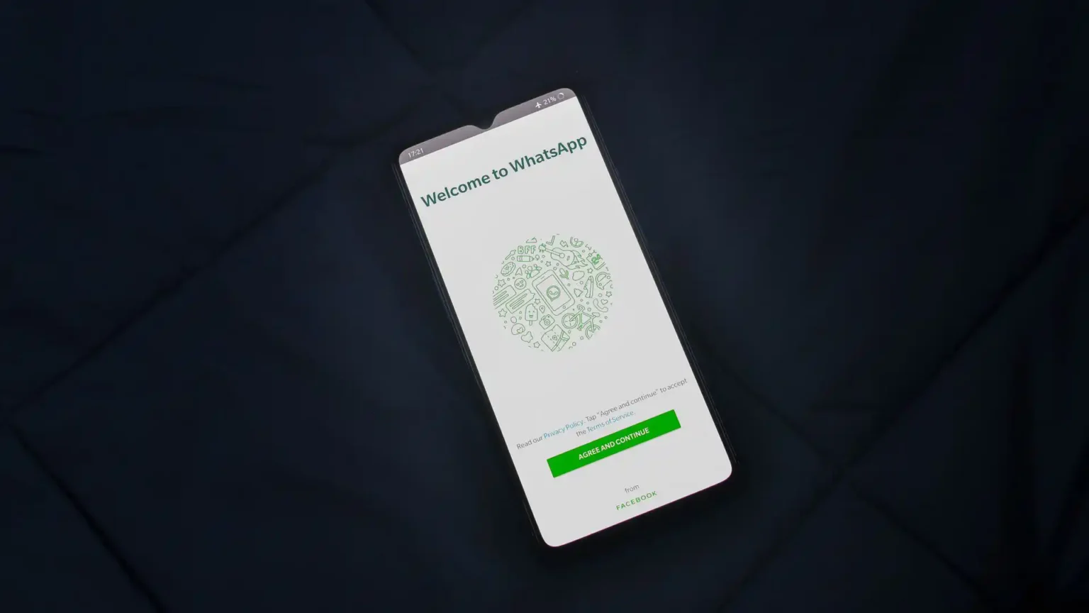 Smartfón s otvorenou uvítacou obrazovkou aplikácie WhatsApp položený na tmavom povrchu.