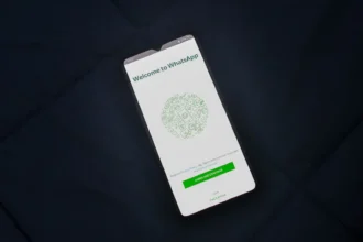 Smartfón s otvorenou uvítacou obrazovkou aplikácie WhatsApp položený na tmavom povrchu.