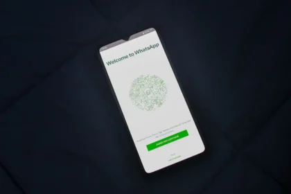 Smartfón s otvorenou uvítacou obrazovkou aplikácie WhatsApp položený na tmavom povrchu.