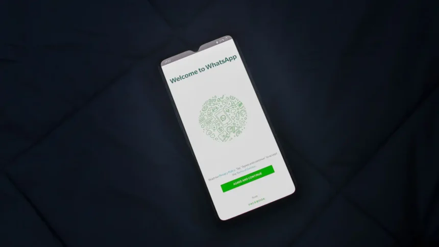 Smartfón s otvorenou uvítacou obrazovkou aplikácie WhatsApp položený na tmavom povrchu.