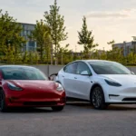 Červená Tesla Model 3 a biela Tesla Model Y stoja vedľa seba pri nabíjacích staniciach v modernom mestskom prostredí.